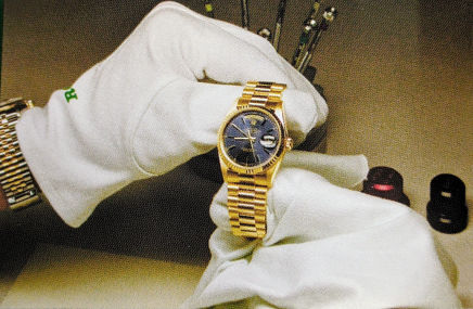 Hands wearing white glows holding gold Rolex watch.